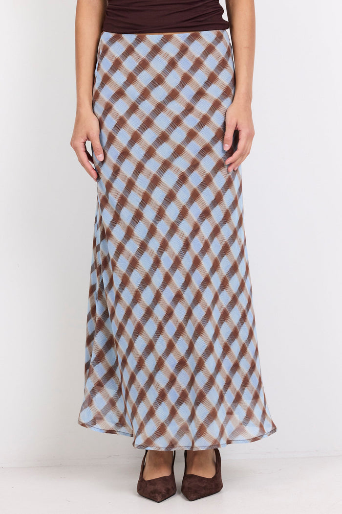 A model wearing a brown and light blue checkered maxi skirt with a dark brown top and brown pointed-toe heels, standing against a plain white background.