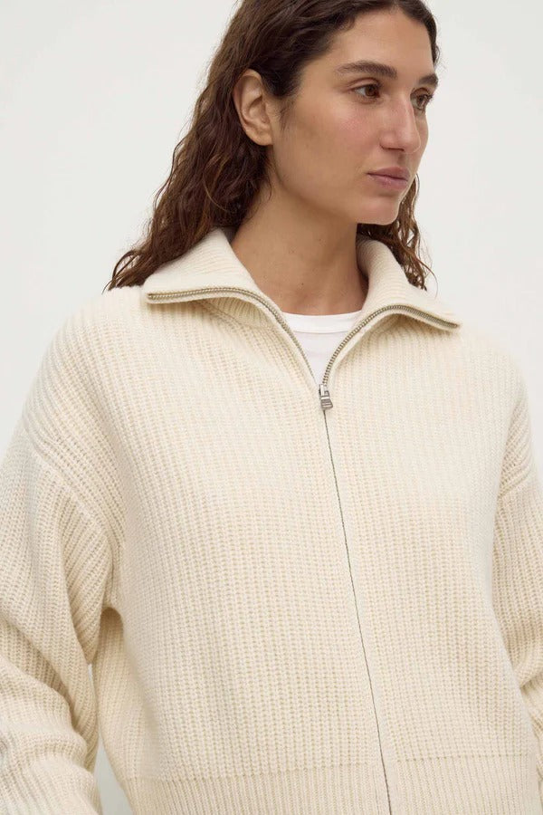 Person wearing a cream-colored zip-up sweater against a plain background