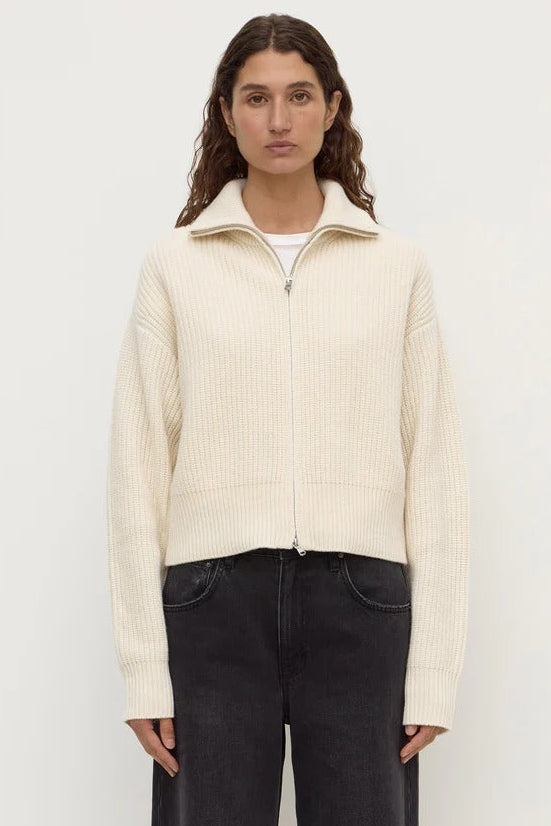 Woman wearing a cream ribbed sweater over a white shirt with black pants on a white background