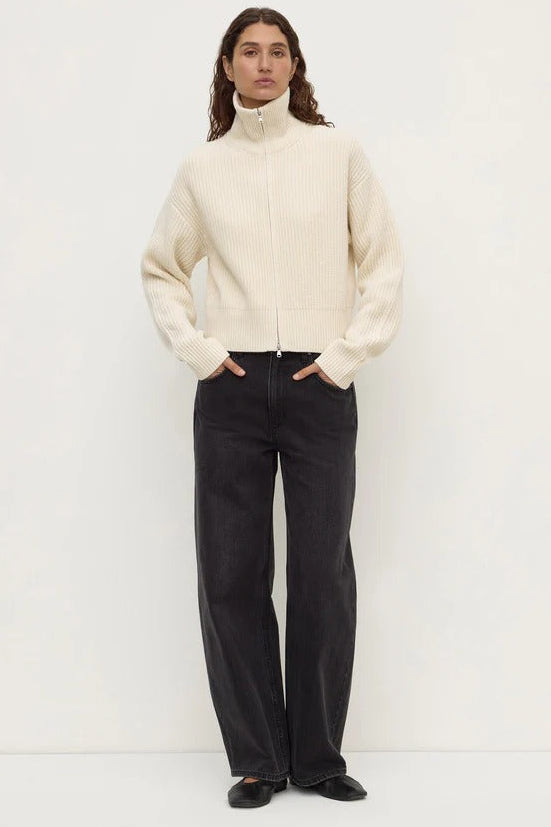 Person wearing a cream sweater and black pants on a white background