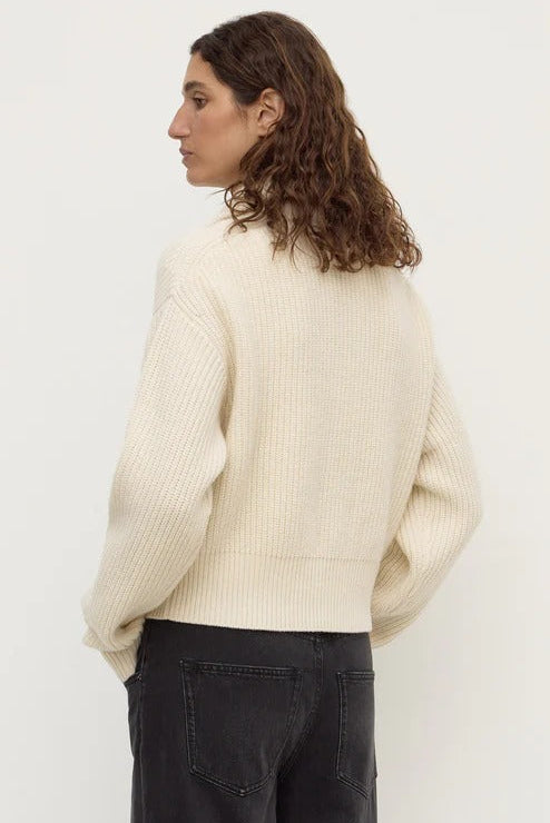 Person wearing a cream sweater and dark pants against a white background