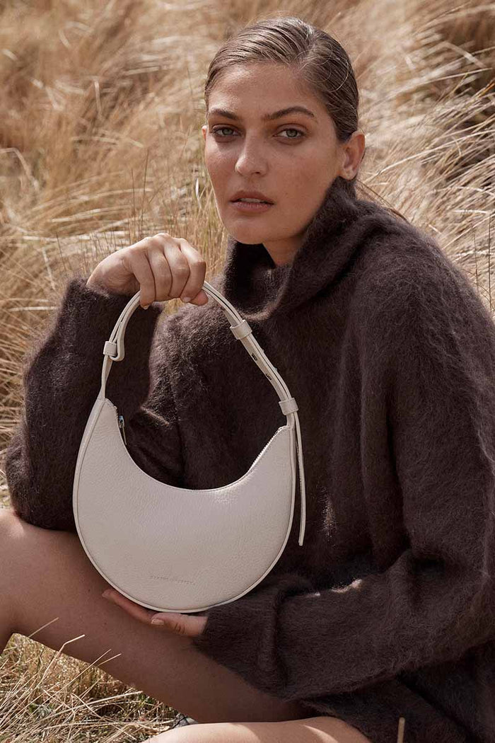 Woman holding a white handbag in a field of tall grass