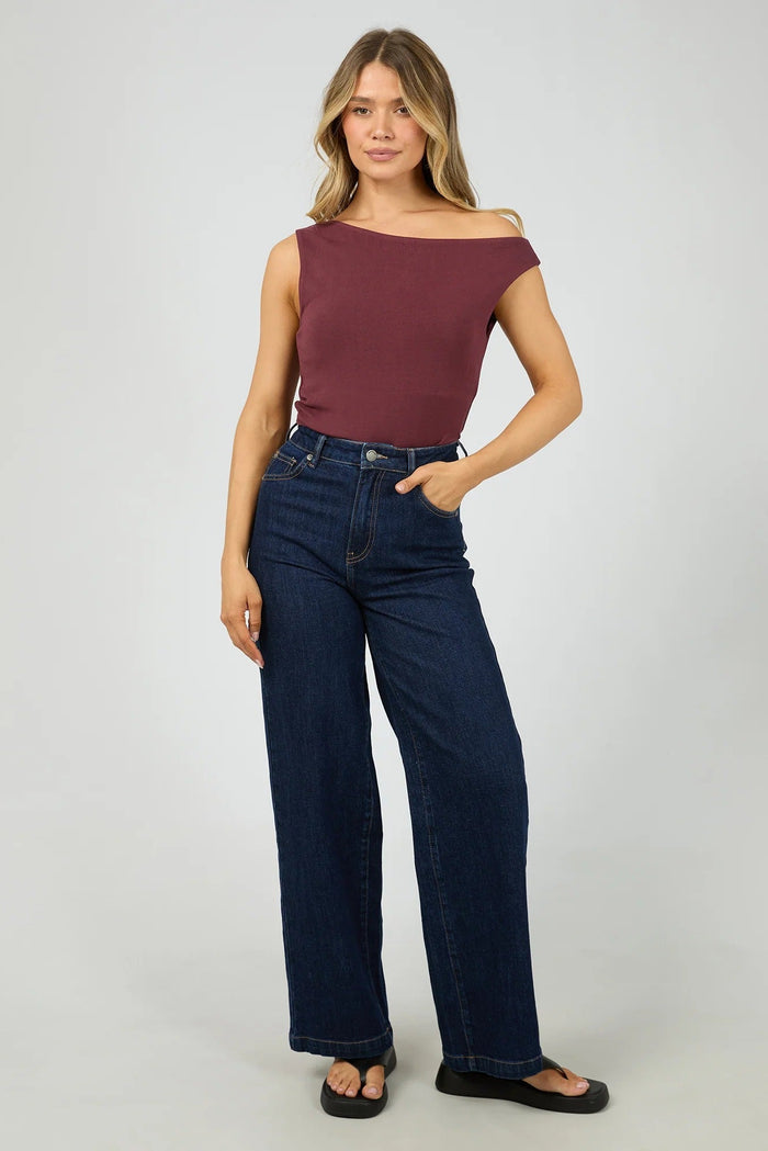 Woman wearing a burgundy top and dark blue jeans on a white background