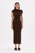 A woman modeling a dark brown off-the-shoulder midi dress with a draped neckline and side tie detail, paired with dark brown heeled sandals, against a plain white studio background.