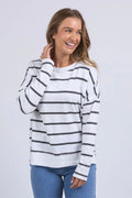 Woman wears a white long sleeve top with black horizontal stripes, crew neck, exposed stitching, and a relaxed fit. Styled with blue jeans for a casual, easy-going look.
