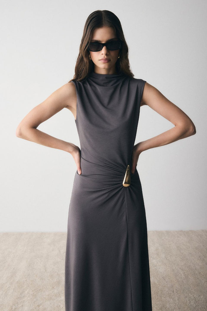 Woman wearing a dark gray sleeveless dress with a belt against a plain background