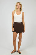 Woman wearing a white tank top and brown skirt on a plain background