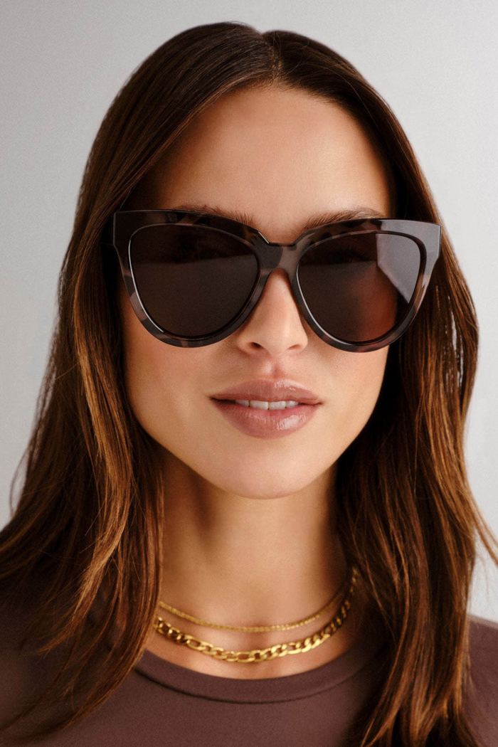 model wears Front-facing view of oversized cat-eye sunglasses in a glossy tortoiseshell frame with warm brown lenses. The bold, sculpted silhouette adds a vintage-inspired edge with a modern twist.