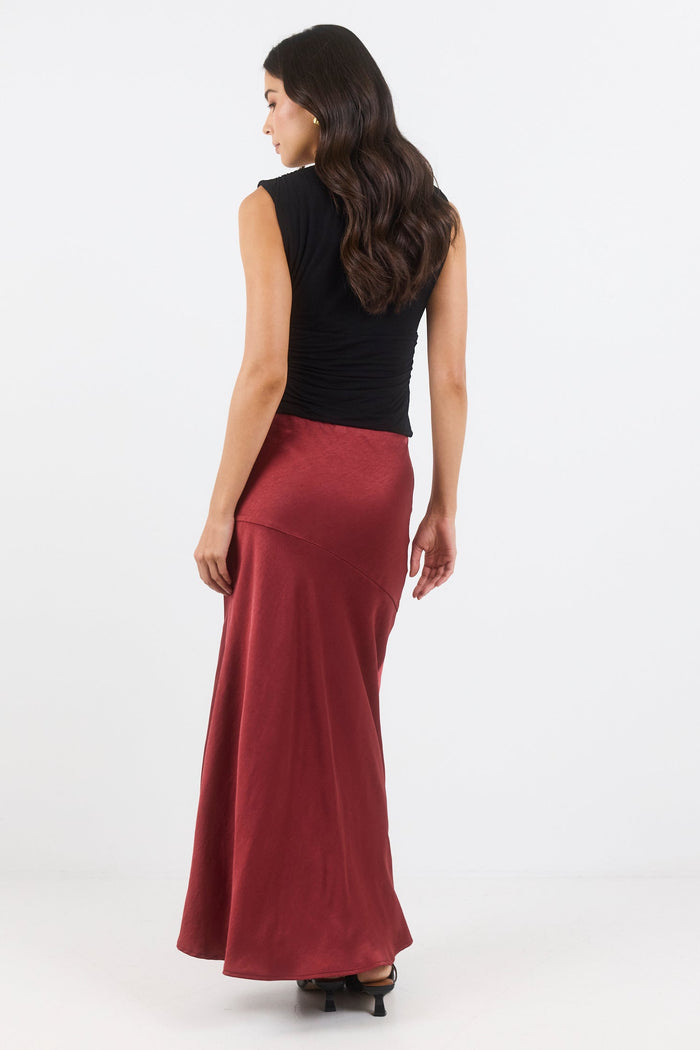 Woman wearing a black top and burgundy skirt on a white background