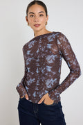 Woman wearing a long sleeve brown and blue tie-dye mesh top with dark jeans, standing with hands in pockets