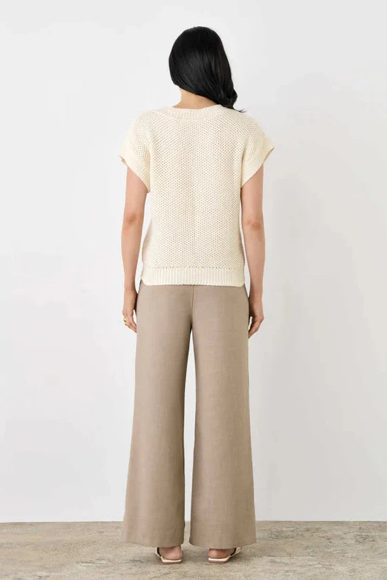 Woman wearing a beige top and wide-leg pants against a white background