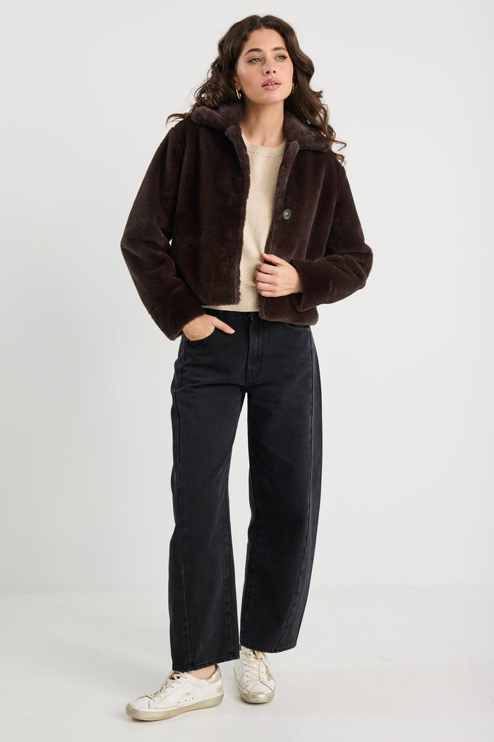 Woman wearing a brown jacket and black pants on a white background