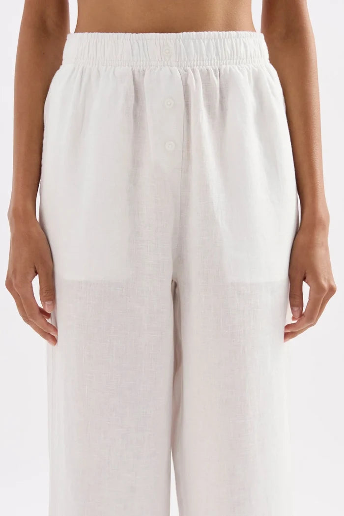 White wide-leg linen pants with an elastic waistband and front button detail, shown on a model against a light gray background.