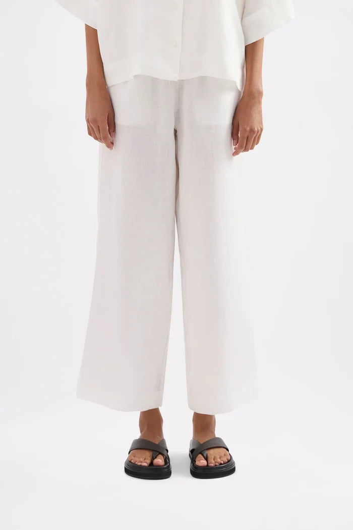 A model wearing white wide-leg cropped pants with a matching white top and black slide sandals, shown from the waist down against a plain white studio background.