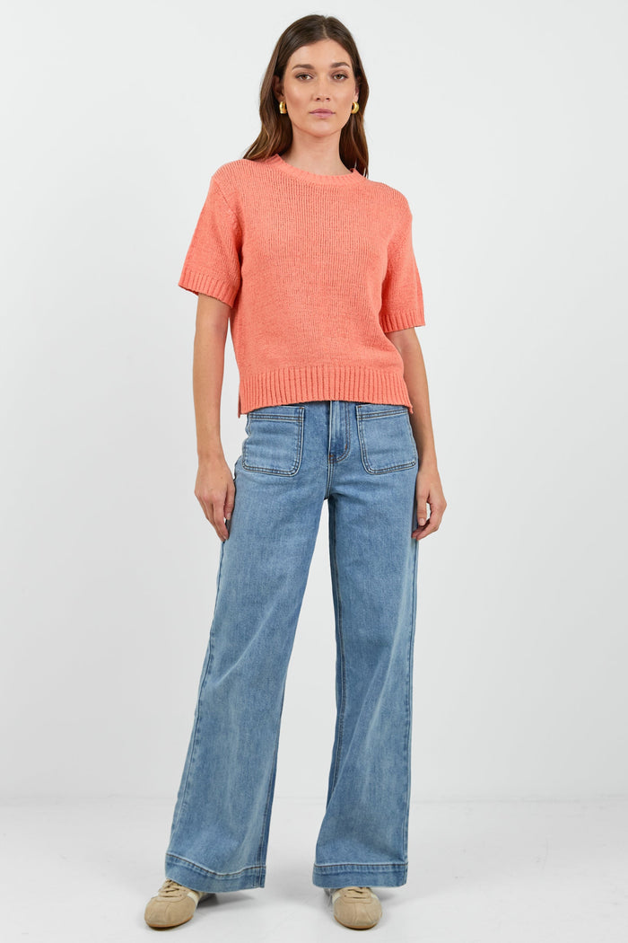 Woman wearing a orange tee and blue jeans on a white background