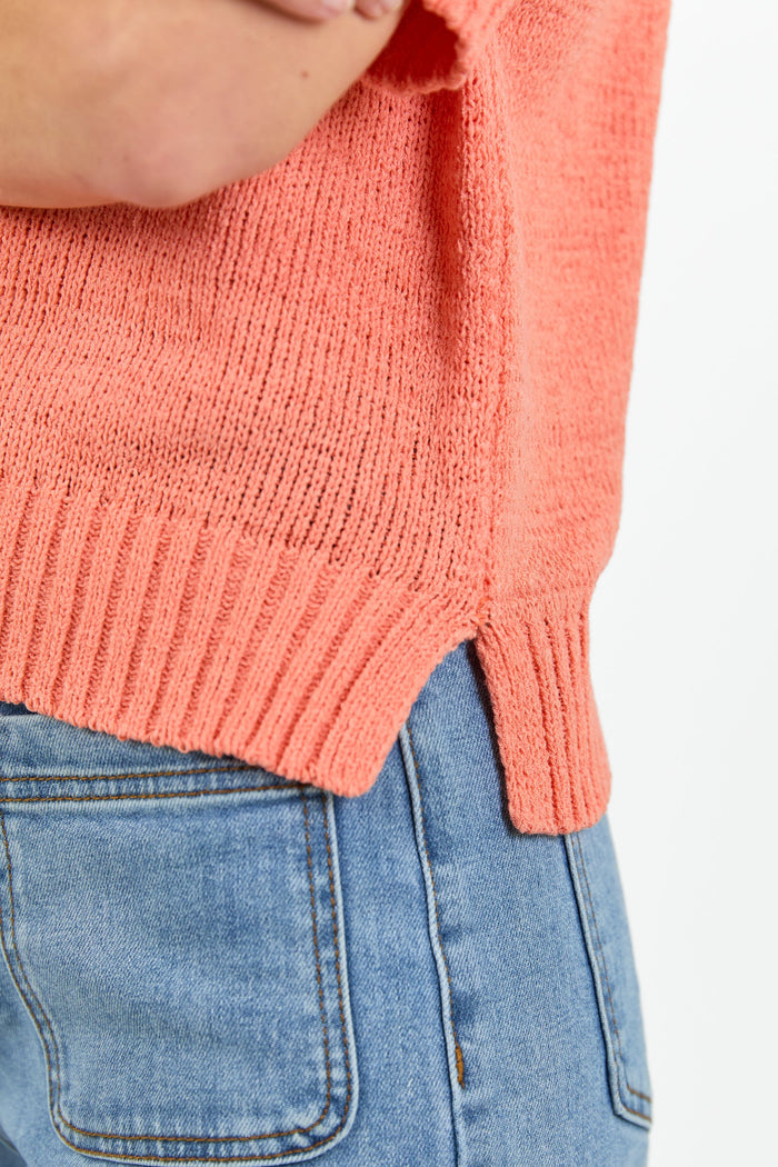 Close up of an orange tee side hem split detail and blue jeans on a white background