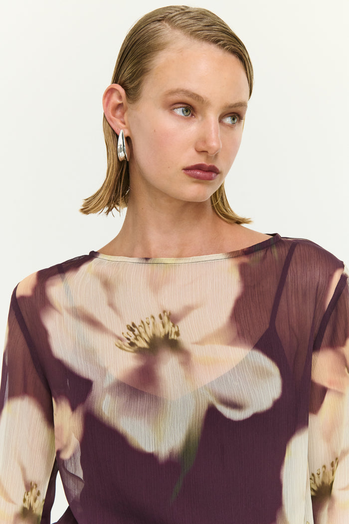 Woman wearing a sheer blouse with floral design on a plain background