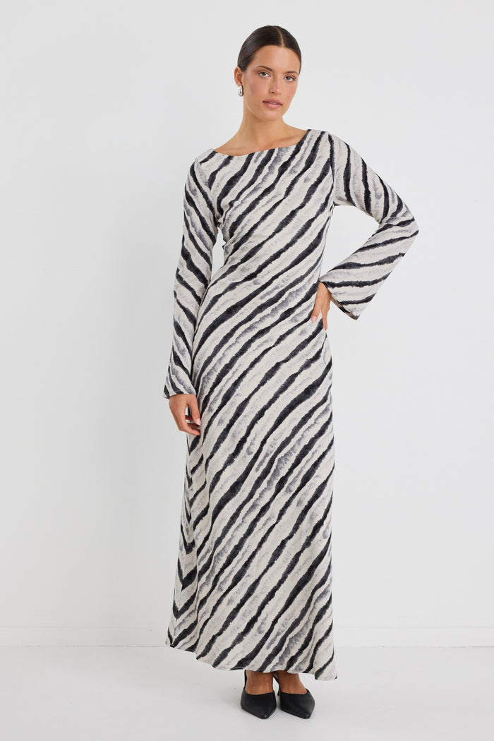 Woman wearing a full-length bias-cut dress with long sleeves and a diagonal charcoal stripe print, styled with black pointed heels.