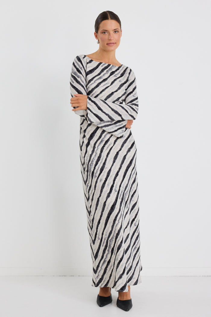 Woman wearing a full-length bias-cut dress with long sleeves and a diagonal charcoal stripe print, styled with black pointed heels.