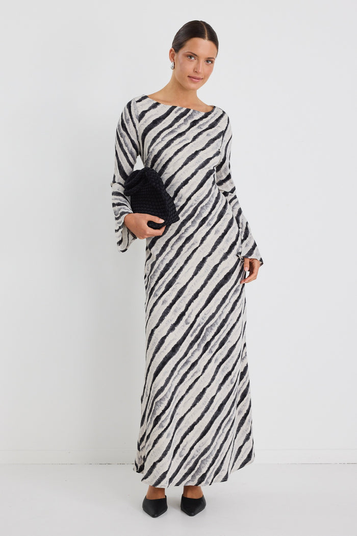 Woman wearing a full-length bias-cut dress with long sleeves and a diagonal charcoal stripe print, styled with black pointed heels.