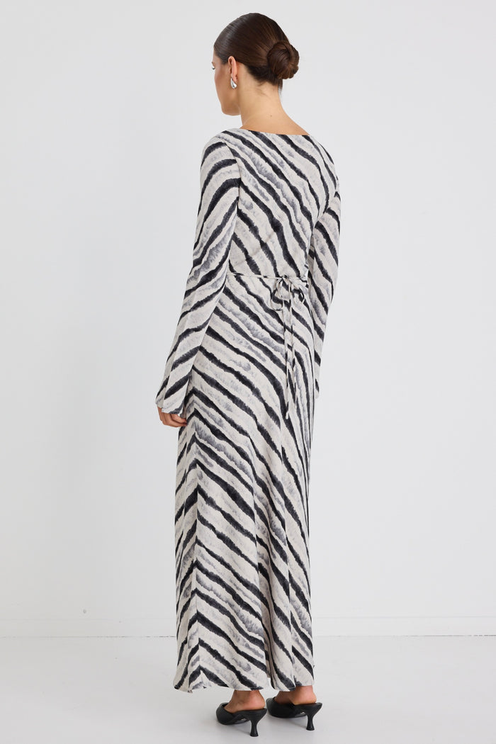 Woman wearing a full-length bias-cut dress with long sleeves and a diagonal charcoal stripe print, styled with black pointed heels.