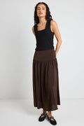 A woman wearing a flowing espresso-coloured hammered satin skirt with soft gathers, styled with a black top and textured flats.