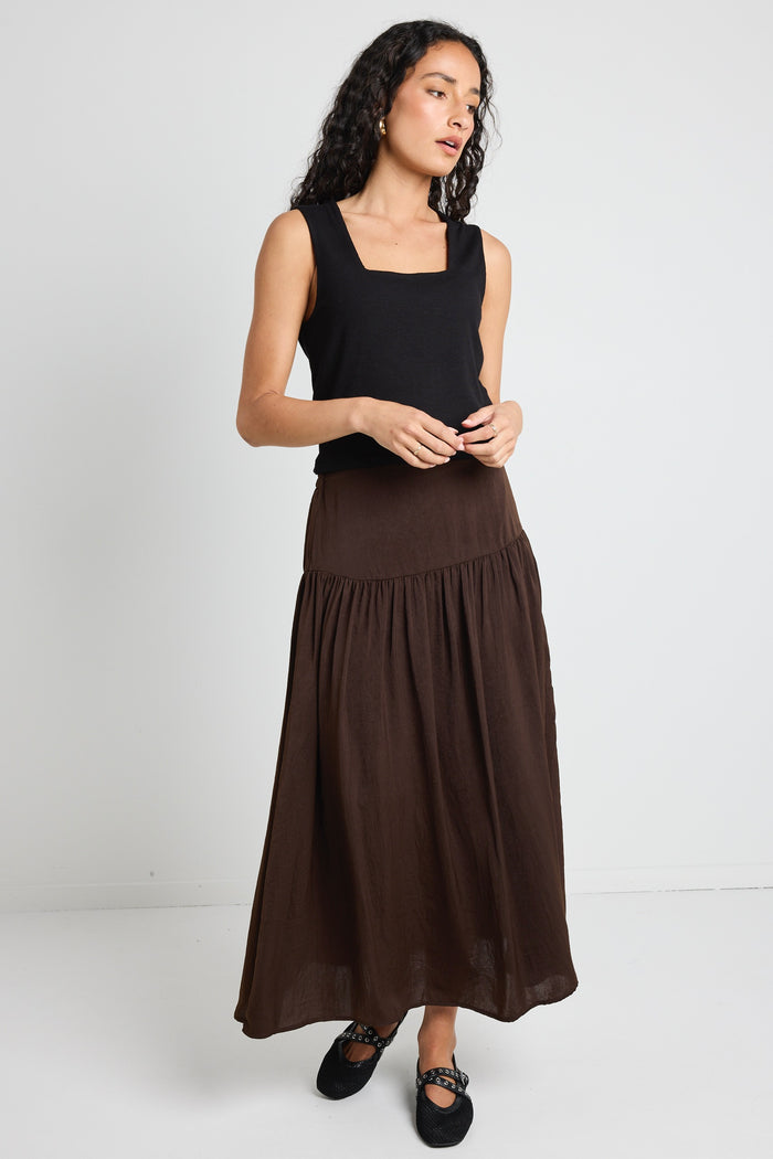 A woman wearing a flowing espresso-coloured hammered satin skirt with soft gathers, styled with a black top and textured flats.