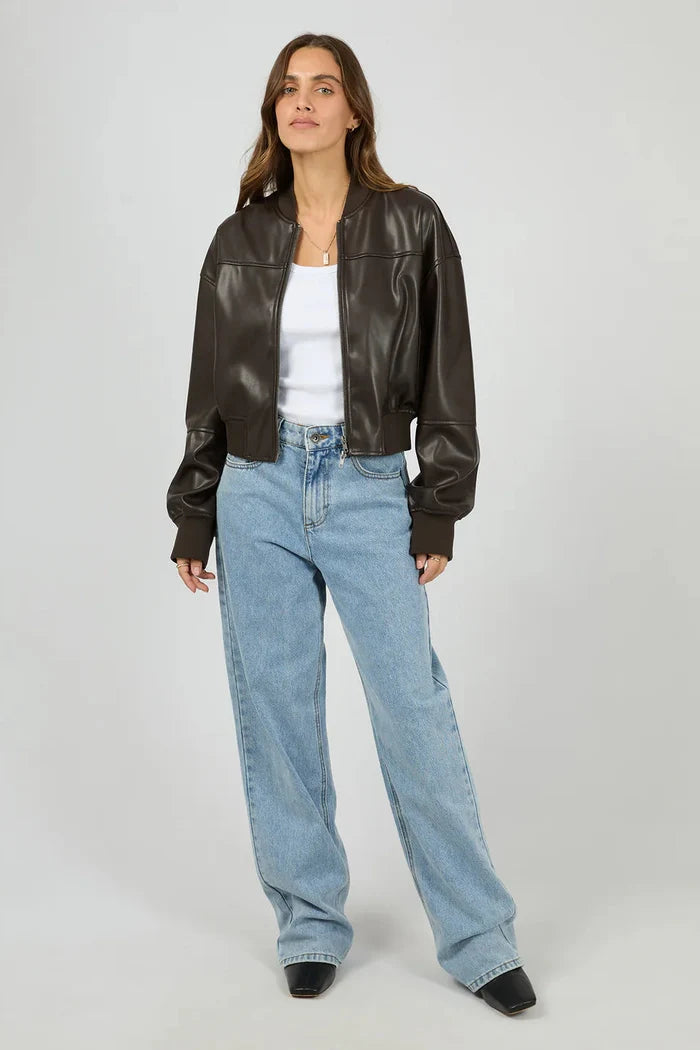 Woman wearing a brown leather jacket and blue jeans on a white background