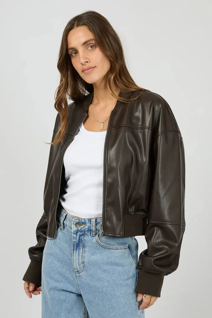 Woman wearing a black leather jacket over a white shirt and blue jeans on a plain background