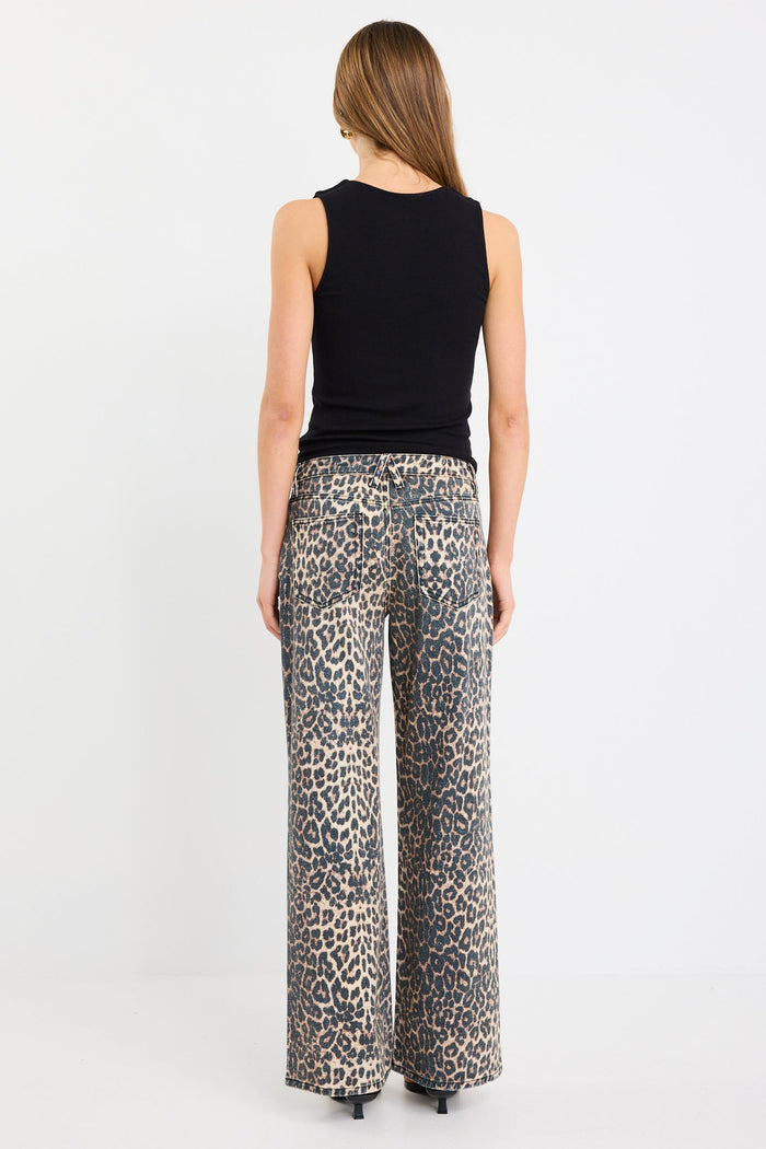 Woman wearing a black sleeveless top and leopard print pants on a white background