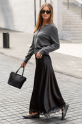 Woman in a gray sweater and black skirt walking on a sidewalk.