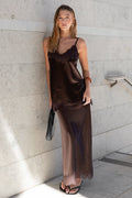 Woman in a brown satin dress standing against a light gray wall.