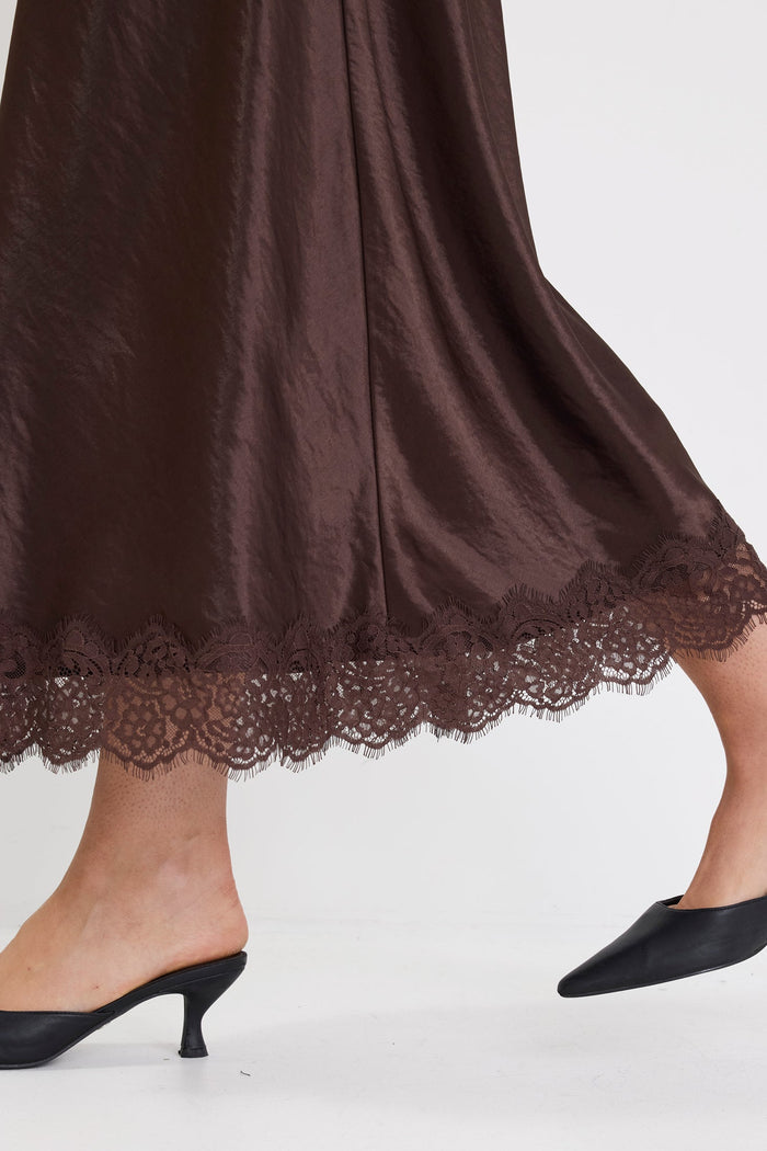 Black high-heeled shoes worn with a dark brown lace-trimmed skirt on a white background