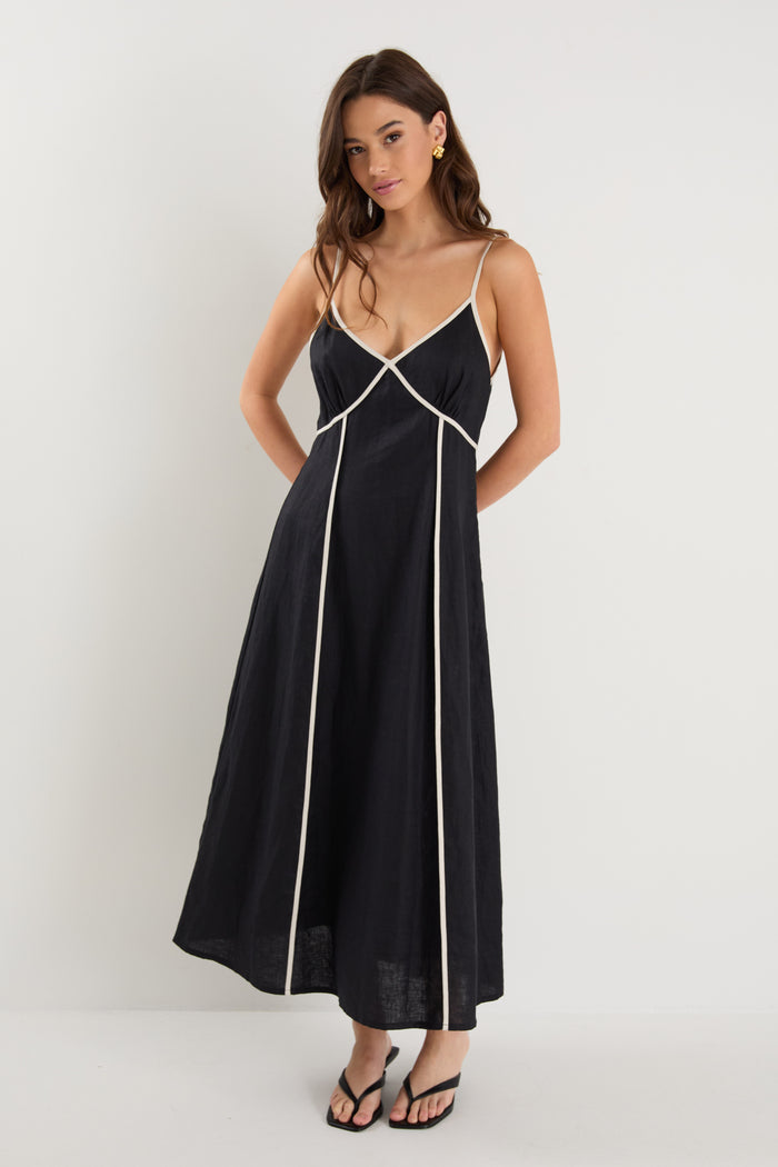 Woman wearing a black linen strappy dress with white contrast trim, fully lined, styled with black heeled sandals.