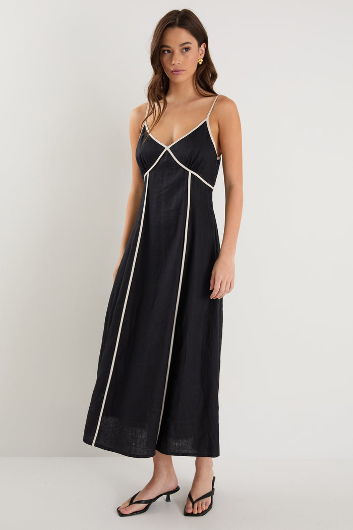 Woman wearing a black linen strappy dress with white contrast trim, fully lined, styled with black heeled sandals.