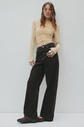 Woman wearing a beige top and black pants against a white background