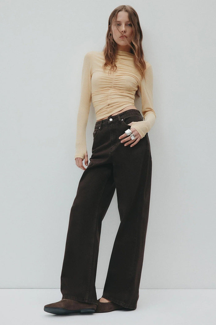 Woman wearing a beige top and black pants against a white background