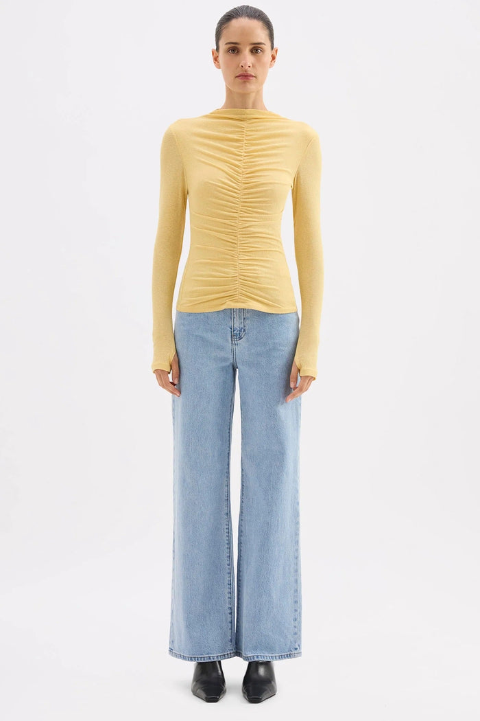 Woman wearing a yellow ruched sweater and light blue jeans on a white background