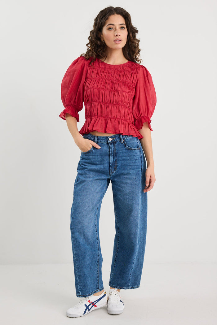 Woman wearing a red blouse and blue jeans on a white background