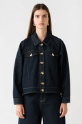 Woman wearing a dark denim jacket and pants on a white background