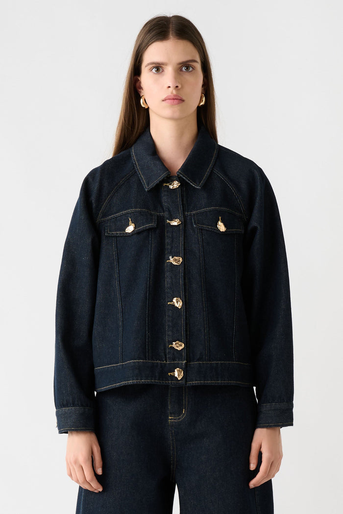 Woman wearing a dark denim jacket and pants on a white background