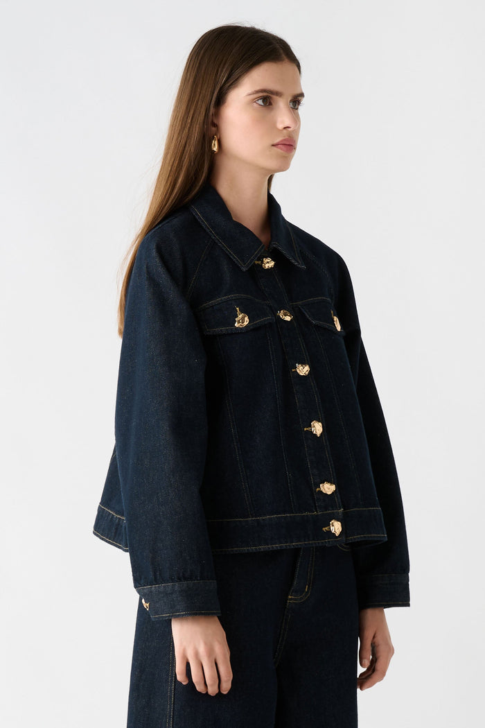 Woman wearing a dark denim jacket and pants on a white background