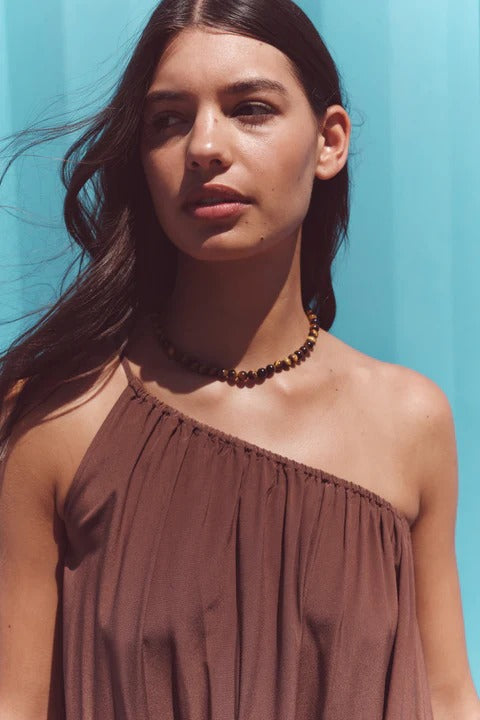 Woman wearing a brown one-shoulder top against a blue background