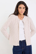 Woman wearing a beige cable knit cardigan over a white shirt with blue jeans on a white background