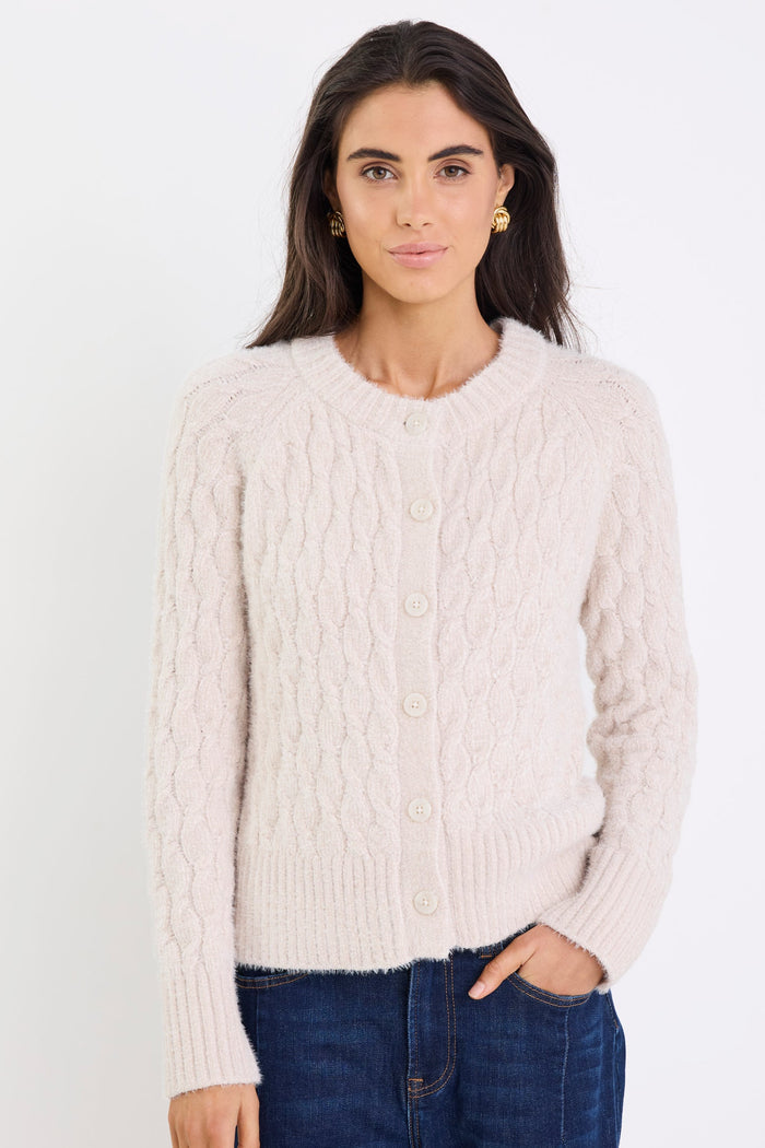 Woman wearing a cream cable knit cardigan against a white background