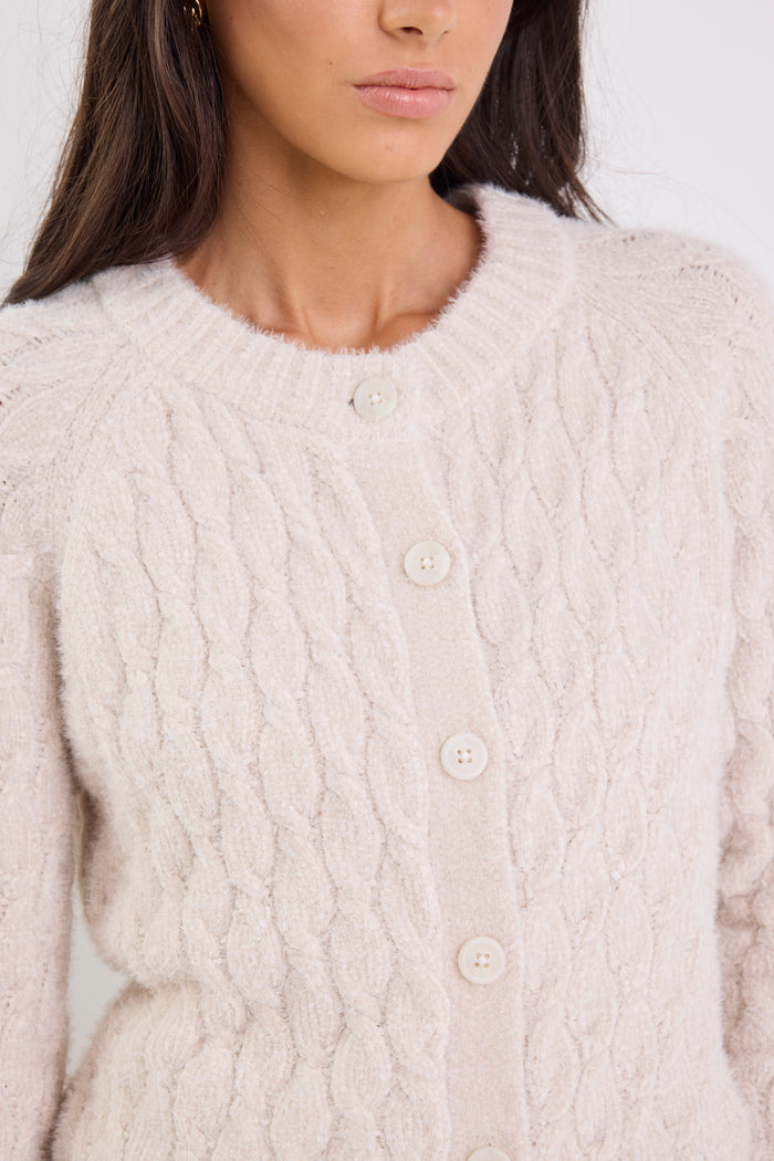 Close-up of a person wearing a light pink cable knit cardigan with button details.