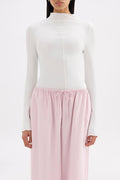A model wearing a white long-sleeve mock neck top and light pink drawstring lounge pants against a plain white background.