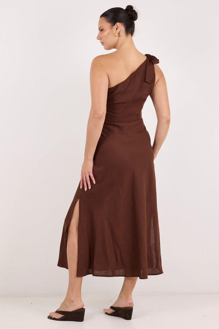 A woman modeling a brown one-shoulder midi dress with a side slit, shown from the back against a plain white studio background.