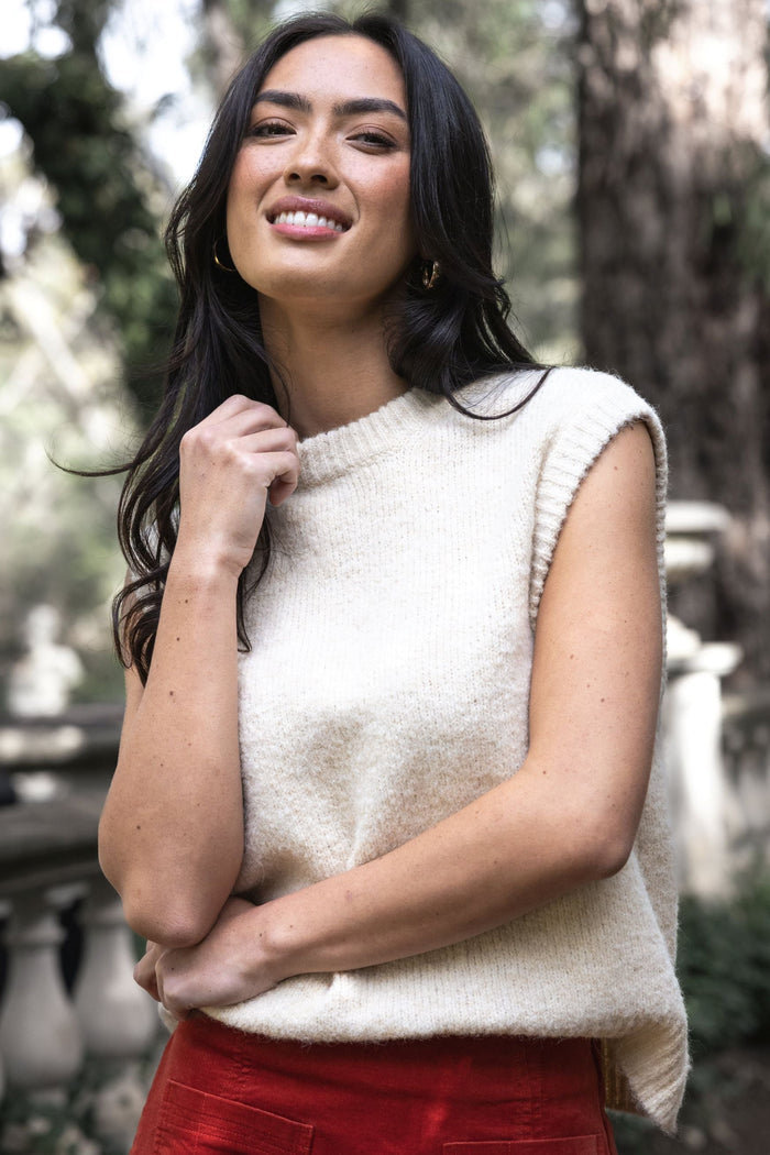 Woman wearing a cream sleeveless sweater and red skirt outdoors
