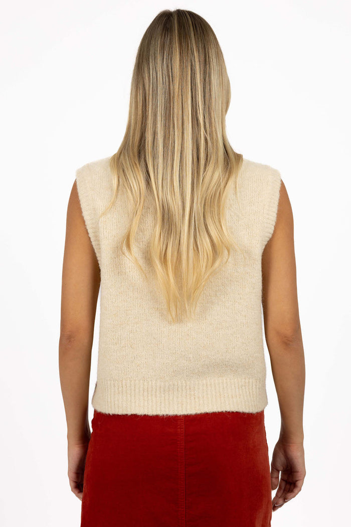 Person wearing a beige sleeveless sweater over a red skirt on a white background